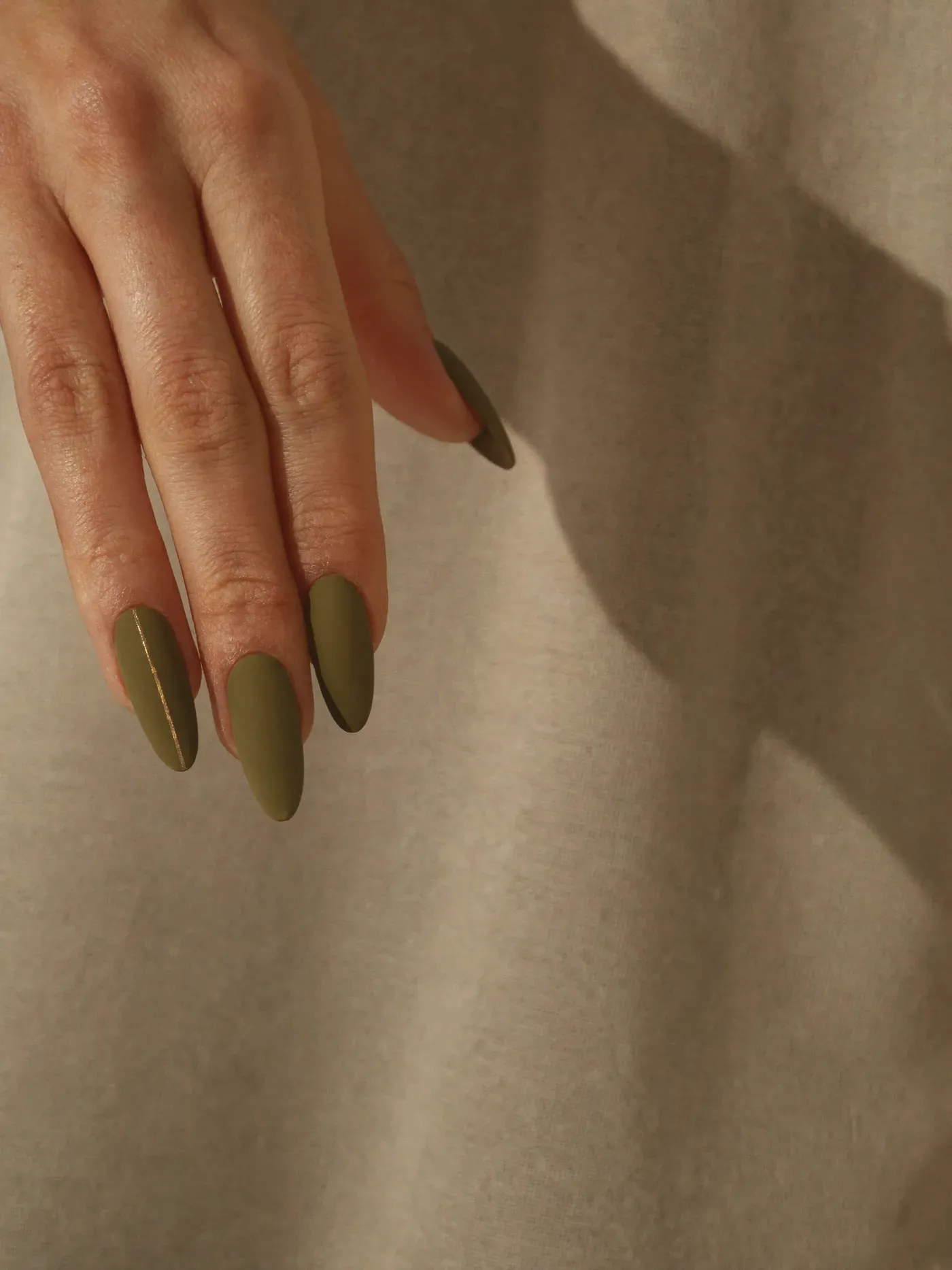 Detail of minimalist nail art in olive green with a fine gold line